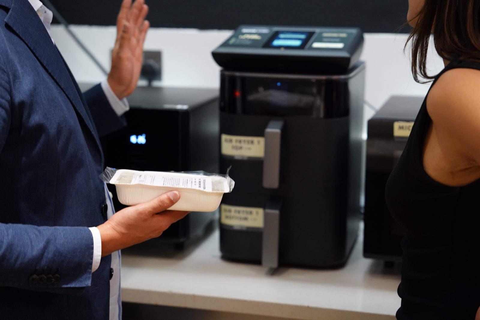 A member of staff holding a Nova Chef meal pack in front of the air fryer and scan-to-cook station